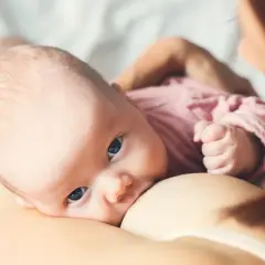 Niemowlę karmione piersią, z uwagą wpatrujące się w obiektyw. To piękny okres macierzyństwa.