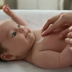Delikatna pielęgnacja 12 tygodniowego dziecka. Krem na jego skórze, czułe dłonie mamy.