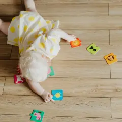 Dziecko z jasnymi włosami, w żółtej sukience w kropki, bawi się na podłodze. Rozrzucone są puzzle ze zwierzątkami i słońcem. To moment, kiedy dziecko zaczyna się obracać.