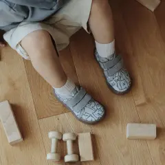 Roczne dziecko bawi się drewnianymi klockami na podłodze. Ma na sobie kapcie w kotki, idealne do chodzenia po domu.