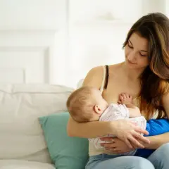 Ciepły moment karmienia piersią. Mama z czułością patrzy na swoje dziecko, które spokojnie je.