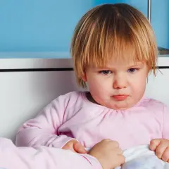 Smutna dziewczynka z nietolerancją laktozy u dzieci, siedzi w łóżku, czuje się źle po wypiciu mleka.