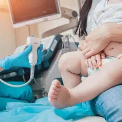 Lekarz wykonuje usg przezciemiączkowe u niemowlaka. Dziecko siedzi na kolanach rodzica, a lekarz trzyma sondę aparatu USG.