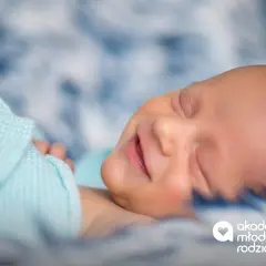 Słodki uśmiech noworodka, kiedy dziecko zaczyna się uśmiechać, otulony błękitnym kocykiem.