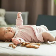 Urocze niemowlę patrzy do góry, leżąc na łóżku z drewnianymi zabawkami.