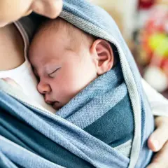 Malutkie dziecko w chuście śpi wtulone w ramiona mamy. Ciepło i bliskość.