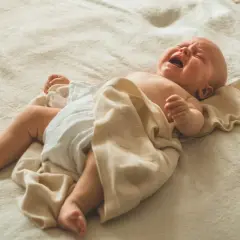 Noworodek leży na plecach, ubrany w pieluszkę, z kocykiem. Jego twarz wykrzywiona jest w płaczu, słychać głośne stękanie noworodka podczas snu.
