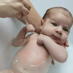 Niemowlę w wanience, delikatnie kąpane. Widać jego pępek, który jest w dobrym stanie, bez oznak problemów.