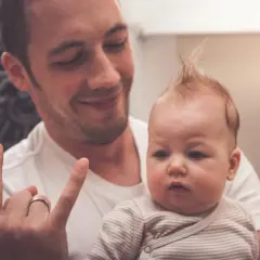 Tata z uśmiechem trzyma dziecko, którego włosy niemowlaka sterczą jak u rockmana.