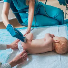 Lekarz wykonuje USG bioderek niemowlaka, sprawdzając, czy nie ma problemów ze strzelającymi stawami.
