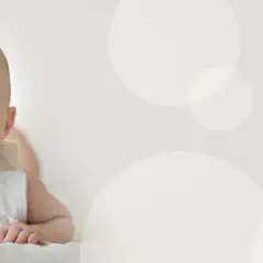 Uśmiechnięte, 4 miesięczne dziecko z niebieskimi oczami leży na brzuchu, patrząc z zaciekawieniem.