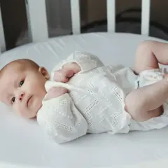 Malutkie stópki dziecka, które dopiero zaczyna widzieć, są delikatnie dotykane przez dłoń rodzica. Leży w białym łóżeczku.