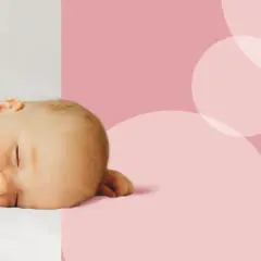 Słodki noworodek śpi spokojnie. Zastanawiasz się, ile śpi noworodek? Ten maluch odpoczywa, otulony białym kocykiem, na tle różowych kółek.