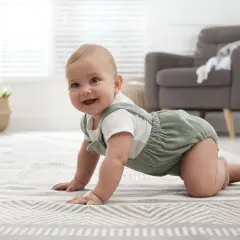 Uśmiechnięte 8 miesięczne dziecko na czworakach odkrywa świat na miękkim dywanie.