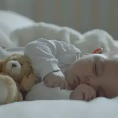 Śpiący noworodek z misiem. Czasem kolki u noworodka a kupka są powiązane, ale teraz maluch odpoczywa.