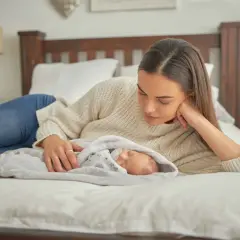 Matka z czułością patrzy na śpiące dziecko, otulone kocykiem. To chwila bliskości i spokoju, idealna na drzemki kontaktowe.