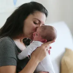 Czuła matka całuje swoje 6 tygodniowe dziecko, trzymając je delikatnie na rękach.
