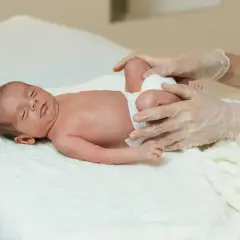 Delikatne badanie niemowlaka, ocena symetrii kończyn. Ręce w rękawiczkach badają nóżki maluszka.