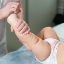Fizjoterapeuta delikatnie masuje nóżkę dziecka, pomagając w leczeniu hipotonia mięśniowa.