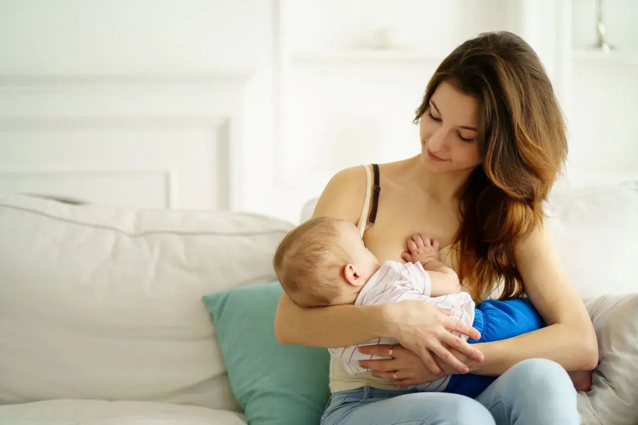 Ciepły moment karmienia piersią. Mama z czułością patrzy na swoje dziecko, które spokojnie je.