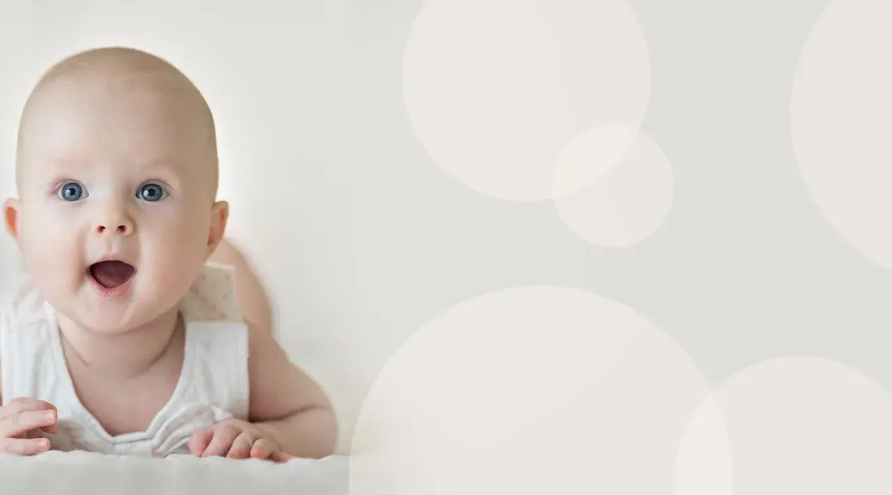Uśmiechnięte, 4 miesięczne dziecko z niebieskimi oczami leży na brzuchu, patrząc z zaciekawieniem.