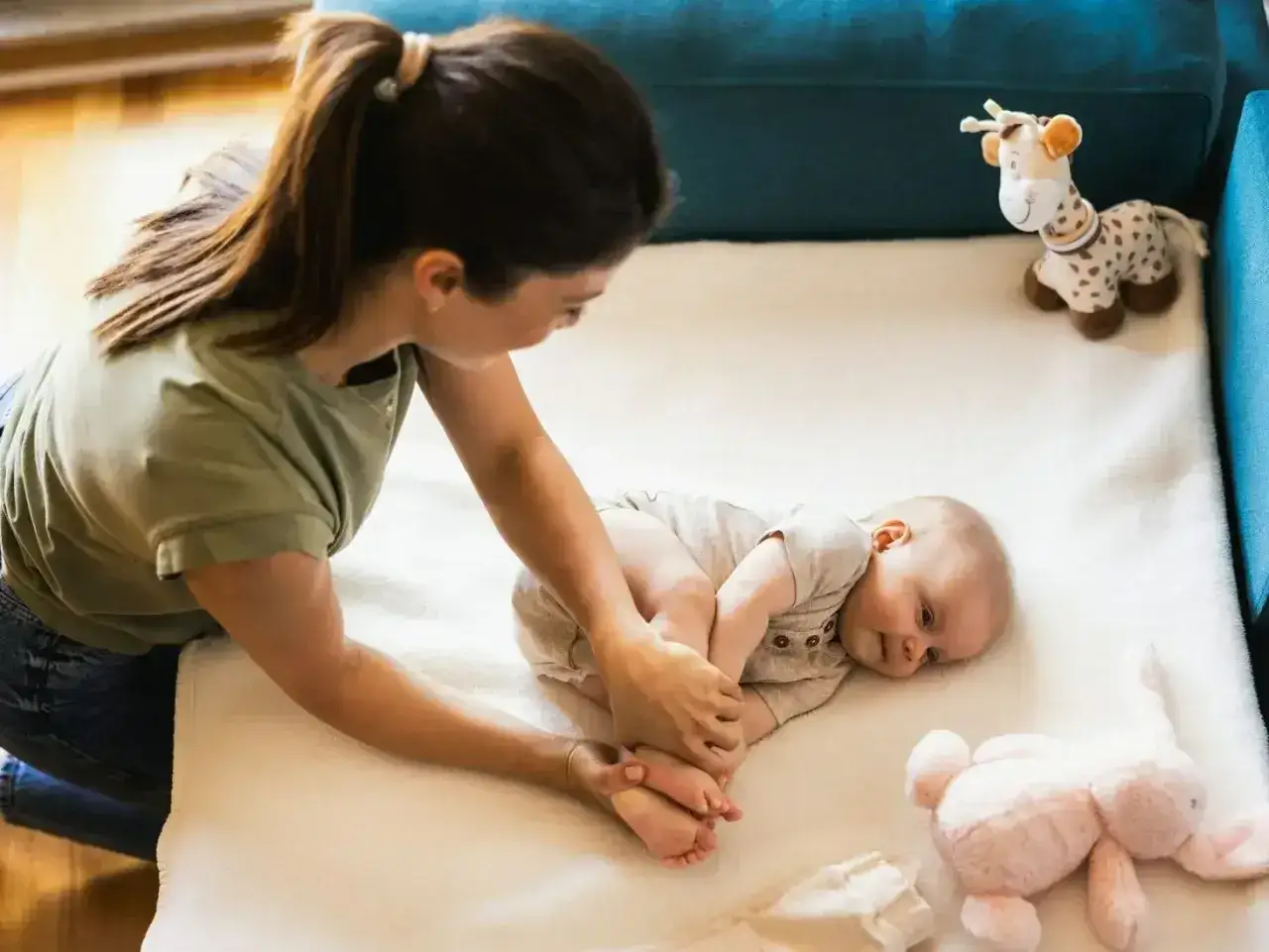 Mama bawi się ze swoim 8-miesięcznym dzieckiem na macie. Obok leżą pluszowe zabawki.
