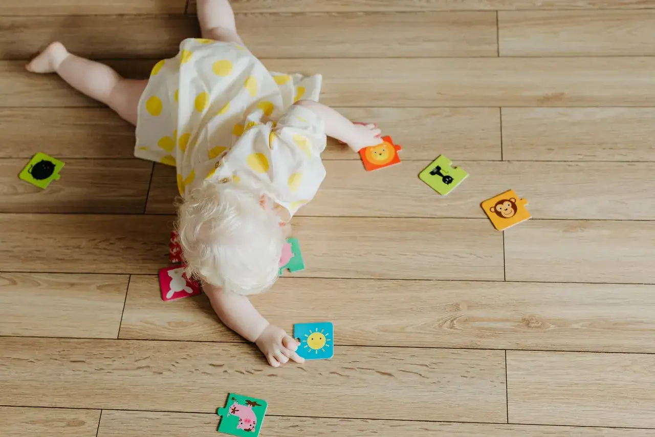 Dziecko w żółtej sukience w kropki odkrywa świat, kiedy zaczyna się obracać. Rozrzucone puzzle z wesołymi zwierzątkami.