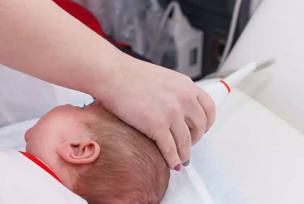 Lekarz wykonuje usg przezciemiączkowe u niemowlaka. Sonda aparatu USG przykładana jest do główki dziecka.