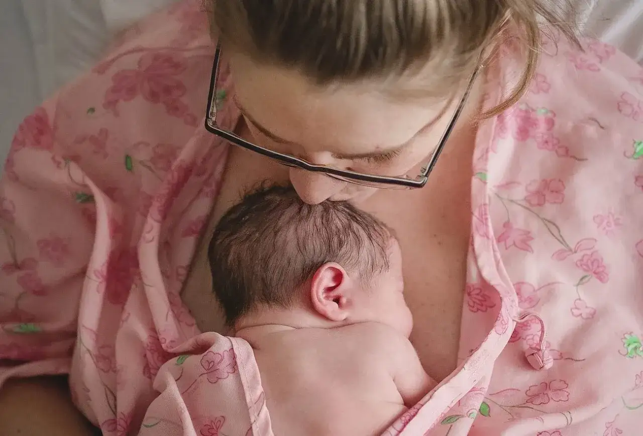 Ciepłe kangurowanie dziecka przez mamę w różowej piżamie w kwiaty. Delikatny pocałunek na główce noworodka.
