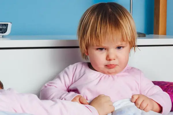 Smutna dziewczynka z nietolerancją laktozy u dzieci, siedzi w łóżku, czuje się źle po wypiciu mleka.